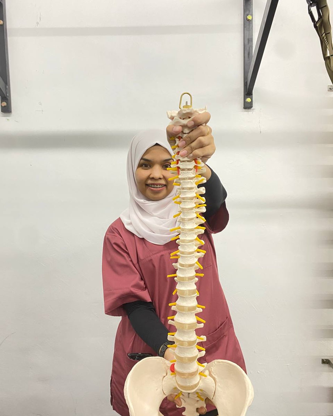 Raja Nazatul holding a spine model to explain slipped disc and back pain to patients at Fisiouzma Kelana Jaya
